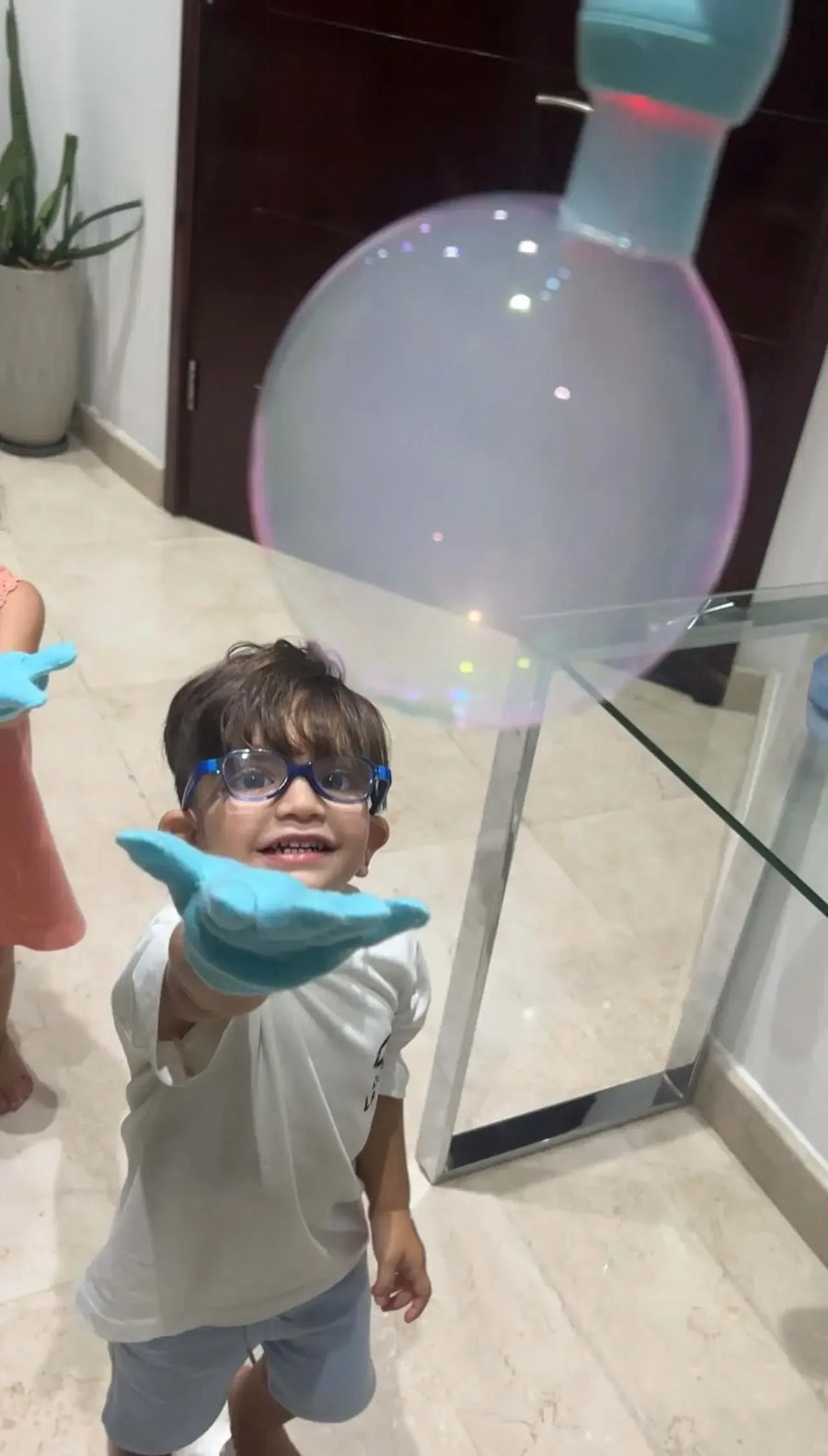 Child wearing protective goggles and a glove watching a smoke-filled bubble from a blue smoke bubble machine
